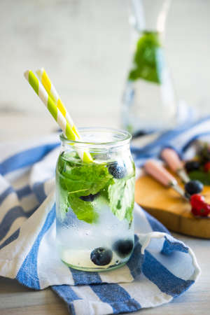 Detox summer drinks with fresh mint leaves and berries on white rustic wooden table