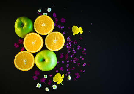 Sliced fresh apple and orange fruits on dark board with flowersの写真素材