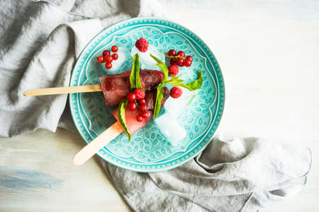 Summer fruit dessert - strawberry lollipops with mint and ice on rustic plate on concrete backgroundの写真素材