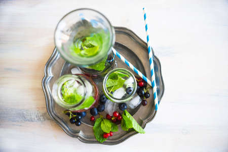 Detox summer drinks with fresh mint leaves and berries on white rustic wooden tableの写真素材