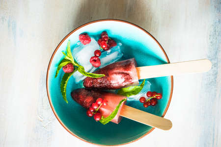 Summer fruit dessert - strawberry lollipops with mint and ice on rustic plate on concrete background