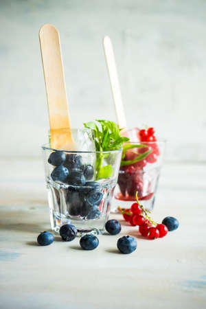 Summer fruit dessert - bilberry and strawberry lollipops with mint and ice on rustic plate on concrete backgroundの写真素材