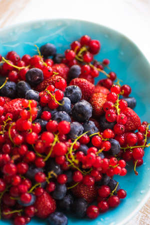 Plate with fresh organic berries - strawberry, blueberry (bilberry) and redcurrant on rustic wooden table with copyspaceの写真素材