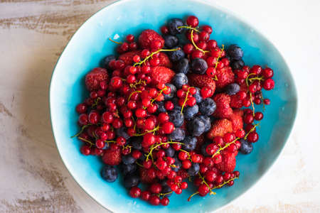 Plate with fresh organic berries - strawberry, blueberry (bilberry) and redcurrant on rustic wooden table with copyspaceの写真素材