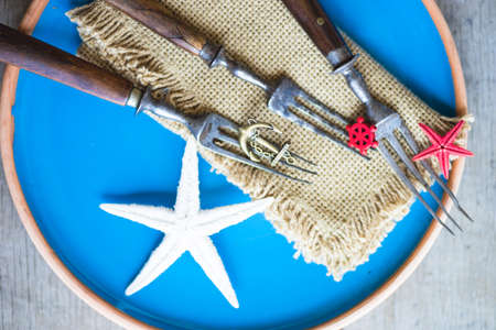 Summer vacation marine table setting with rustic plates and silverware on wooden background with copyspaceの写真素材