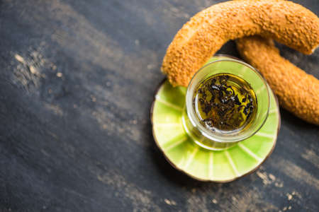 Glass of tea and traditional turkish snack - simit, on dark wooden table