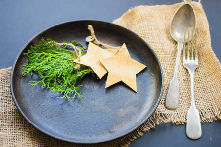 Table setting for festive Christmas dinner on dark wooden table with vintage plates and silverwareの写真素材
