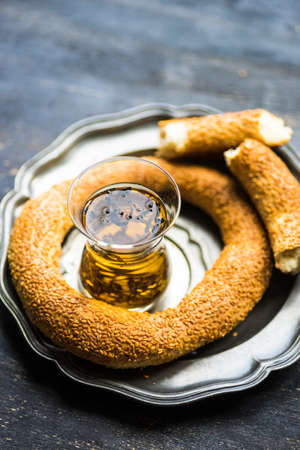 Glass of tea and traditional turkish snack - simit, on dark wooden tableの写真素材