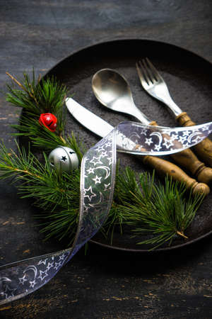 Table setting for festive Christmas dinner on dark wooden table with vintage plates and silverwareの写真素材