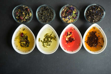 Different types of tea, green tea, peony and ginger tea, rose bud and wild flowers tea on dark wooden background with copyspaceの写真素材