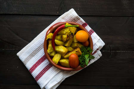 Organic fried potatoes with chillipepper, cherry tomatoes and basil herb in a pan on rustic wooden tableの写真素材