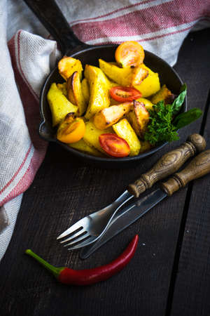 Organic fried potatoes with chillipepper, cherry tomatoes and basil herb in a pan on rustic wooden...