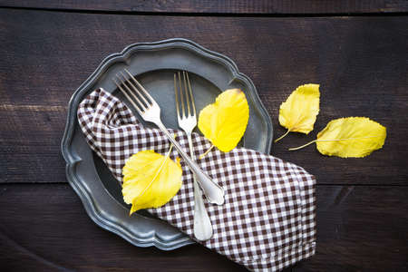 Autumnal table setting with bright yellow leaves and rustic plates on wooden table