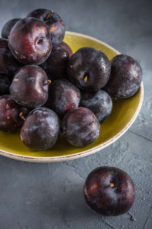 Fresh organic plums in a bowl on grey concrete backgroundの写真素材