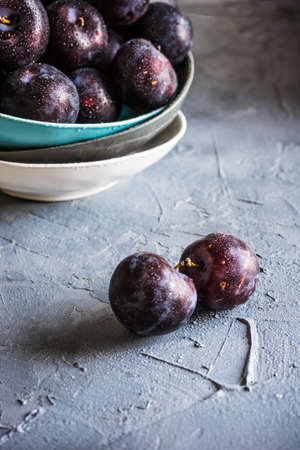 Fresh organic plums in a bowl on grey concrete backgroundの写真素材