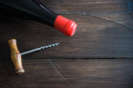 Old vintage corkscrew and bottle of red wine on dark wooden tableの写真素材