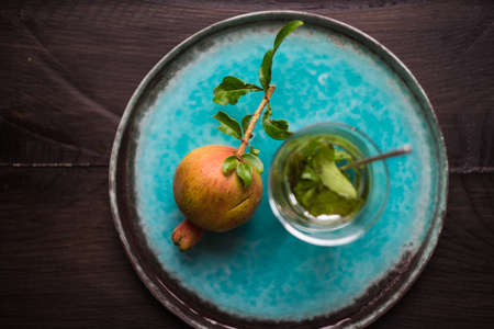 Fresh pomegranate fruit with tree branch on bright plate on dark wooden table