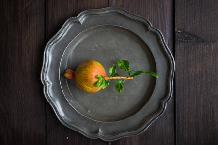 Fresh pomegranate fruit with tree branch on bright plate on dark wooden tableの写真素材