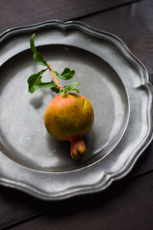 Fresh pomegranate fruit with tree branch on bright plate on dark wooden tableの写真素材