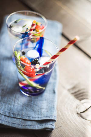 Detox summer drink with rosemary, strawberry, and bilberry with bright color straws on dark wooden tableの写真素材