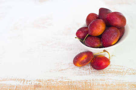 Organic plums in a bowl on white rustic table with copyspace