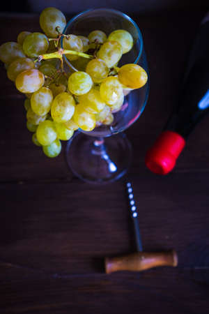 Bottle of wine and wine glass full of ripe grapes on dark wooden tableの写真素材