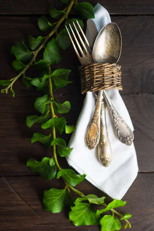 Rustic table setting with vintage ceramic plates and branch of ivy plant on dark old wooden table with copyspaceの写真素材