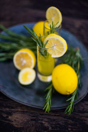 Traditional italian lemon alcohol drink limoncello with pieces of lemon and rosemary herb on dark wooden tableの写真素材