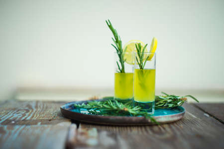 Traditional italian lemon alcohol drink limoncello with pieces of lemon and rosemary herb on dark wooden tableの写真素材