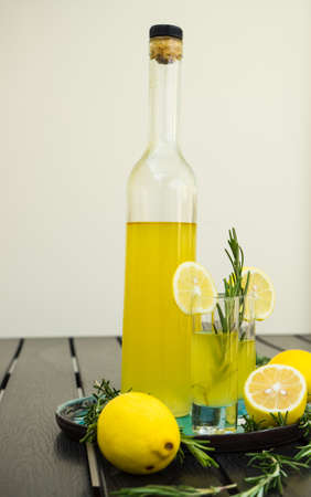 Traditional italian lemon alcohol drink limoncello with pieces of lemon and rosemary herb on dark wooden tableの写真素材