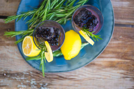 Traditional italian lemon alcohol drink limoncello with pieces of lemon and rosemary herb on dark wooden tableの写真素材