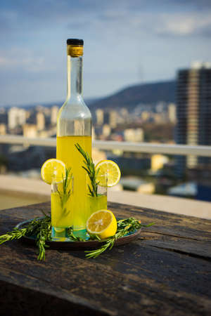 Traditional italian lemon alcohol drink limoncello with pieces of lemon and rosemary herb on dark wooden tableの写真素材