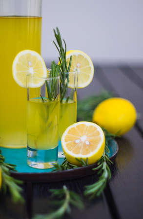 Traditional italian lemon alcohol drink limoncello with pieces of lemon and rosemary herb on dark wooden tableの写真素材