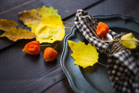Autumnal table setting with bright yellow leaves and physalis  on old wooden table with copyspaceの写真素材