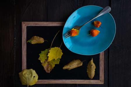 Autumnal table setting with bright yellow leaves and physalis  on old wooden table with copyspaceの写真素材