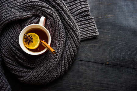 Cup of tea with lemon and winter spices like a cinnamon sticks and anise star with warm  knitted scarf on dark wooden table with copyspaceの写真素材