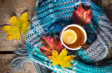 Autumnal concept with cup of tea with lemon, cinnamon stick and anise star on rustic wooden  background full of bright yellow leavesの写真素材