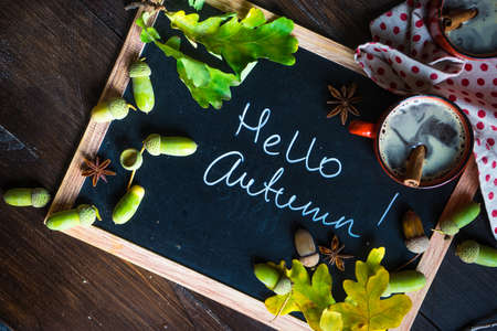 Autumnal concept with mup of coffee with spices, cinnamon stick and anise star on rustic wooden  background full of bright oak yellow leaves and acornsの写真素材