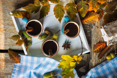 Autumnal concept with mup of coffee with spices, cinnamon stick and anise star on rustic wooden  background full of bright oak yellow leaves and acornsの写真素材
