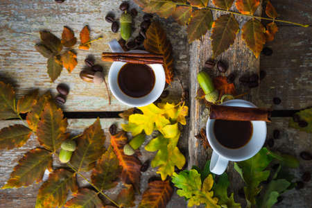Autumnal concept with mup of coffee with spices, cinnamon stick and anise star on rustic wooden  background full of bright oak yellow leaves and acornsの写真素材