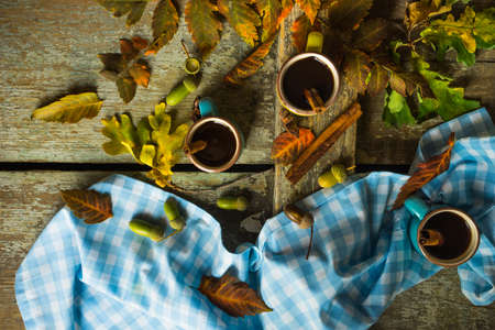 Autumnal concept with mup of coffee with spices, cinnamon stick and anise star on rustic wooden  background full of bright oak yellow leaves and acornsの写真素材