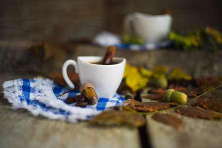 Autumnal concept with mup of coffee with spices, cinnamon stick and anise star on rustic wooden  background full of bright oak yellow leaves and acornsの写真素材