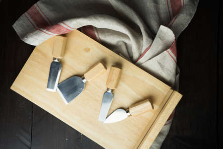 Wooden board and knives for cheese with vintage kitchen towel on rustic wooden tableの写真素材