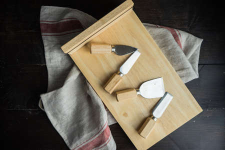 Wooden board and knives for cheese with vintage kitchen towel on rustic wooden tableの写真素材
