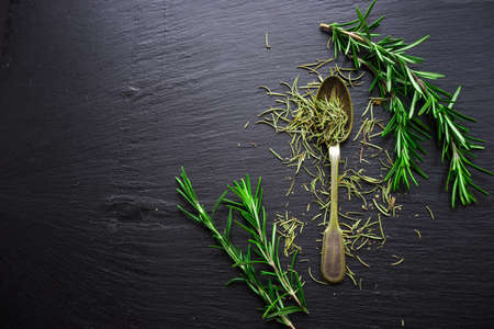 Fresh and dry rosemary spice on black stone board as a organic food conceptの写真素材