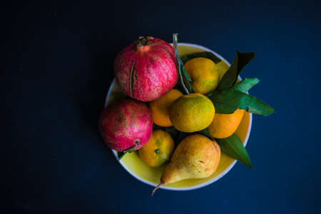 Ripe seasonal fruits - tangerine, pomegranate and pear, in a bowl on dark wooden table with copyspaceの写真素材