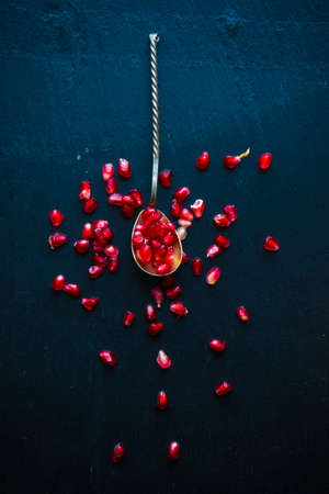 Vintage spoon full of organic pomegranate on black stone board with copyspaceの写真素材