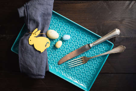 Table setting for festive Easter dinner decorated with easter bunny and eggs on dark wooden table