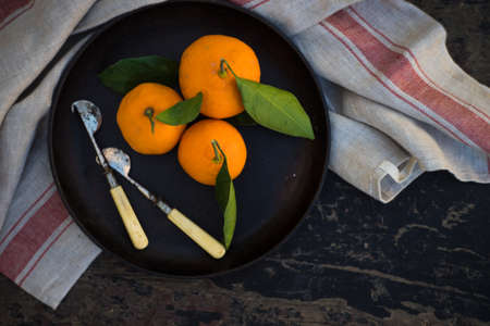 Ripe organic tangerines on rustic plate with knife for citrus on wooden table with copyspaceの写真素材