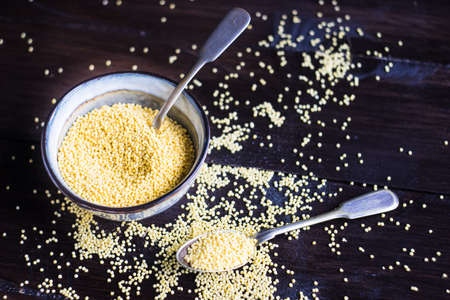 organic raw millet seeds in a rustic bowl on wooden table with copyspaceの写真素材